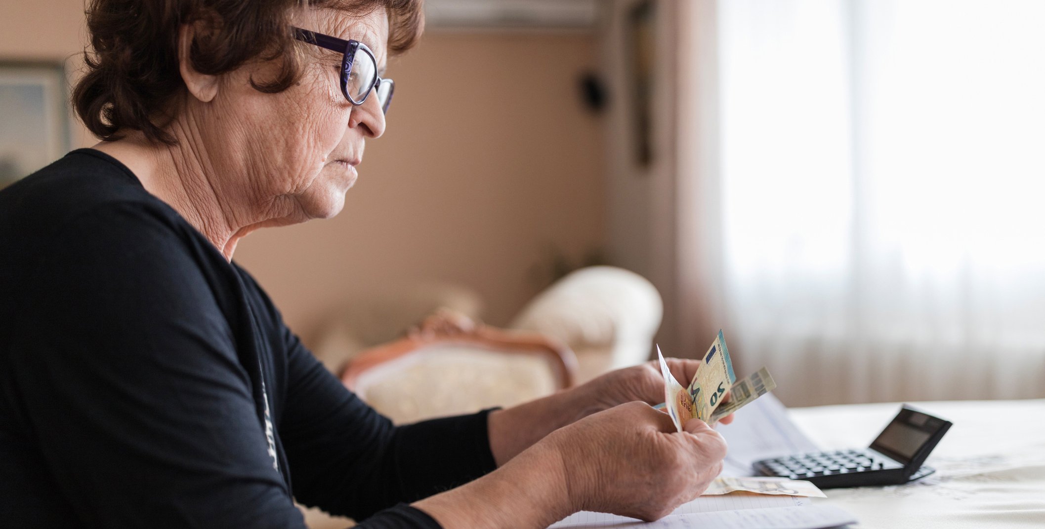 Eine Frau sitzt an einem Tisch und z&auml;hlt Geld, auf dem Tisch liegt ein Taschenrechner